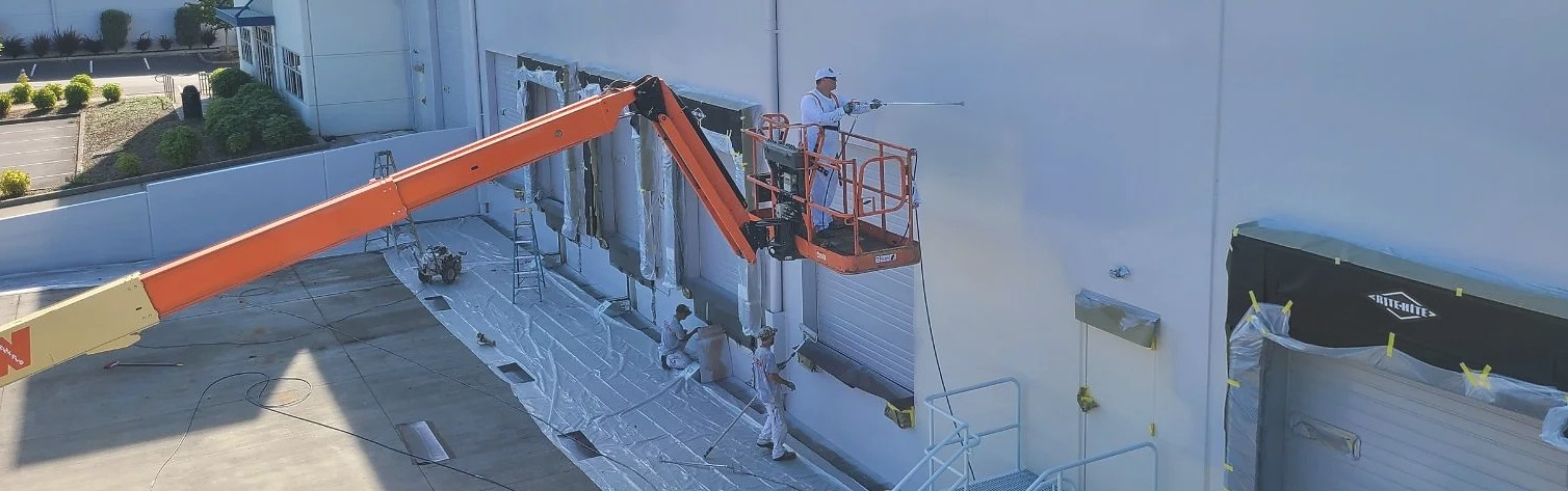 Tri County Painting crew coating a warehouse exterior from a boom lift